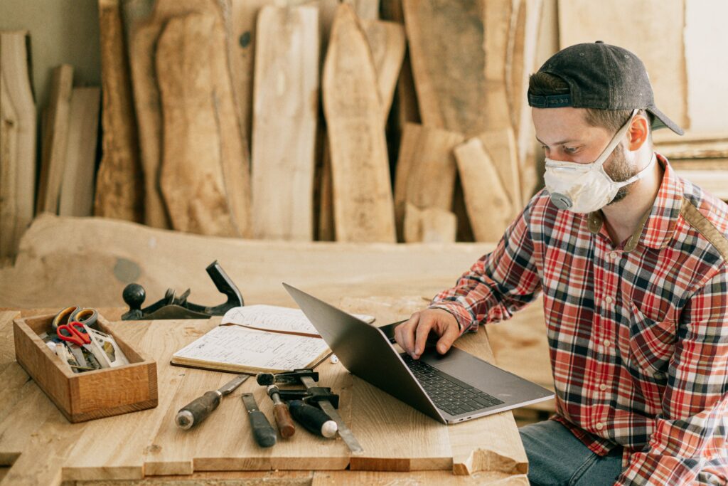 wooden table with tools on, a builder s sat working on a laptop looking frustrated.